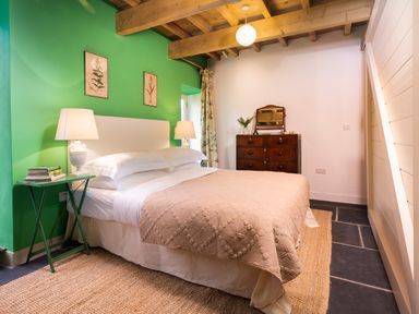 A bedroom with a bed a bedside table with lamps and books a wooden dresser with a mirror at Kentmere Hall Bank Barn Kentmere