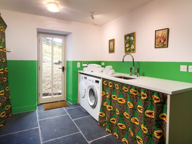 A laundry room with washing machines a sink folded towels a door leading outside and wall art at Kentmere Hall Bank Barn in Kentmere