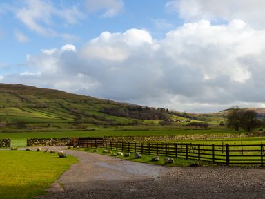 A rural view with green fields stone walls wooden fences and hills under a partly cloudy sky at Kentmere Hall Bank Barn  Kentmere