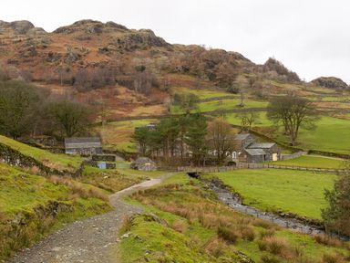A rural scene with a dirt path leading to stone buildings and a small stream at Kentmere Hall Bank Barn Kentmere
