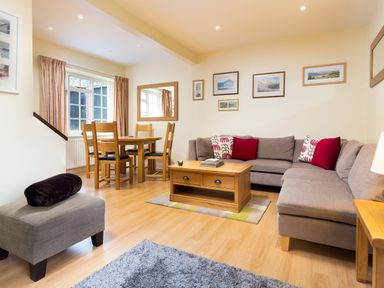 A living room with a gray sectional sofa a wooden coffee table a dining table with chairs and wall art at Scots Pine in Keswick