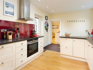 A kitchen with white cabinets a built in oven a stove with a stainless steel hood and a red backsplash at Scots Pine in Keswick