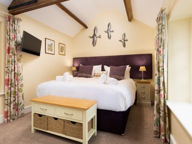 A bedroom with a large bed with rolled towels and pillows bedside tables lamps a chest with baskets a television and floral curtains at Scots Pine in Keswick
