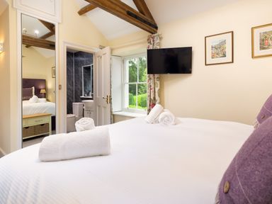 A bedroom with a bed and rolled towels a wall-mounted TV and an open door showing a bathroom at Scots Pine in Keswick