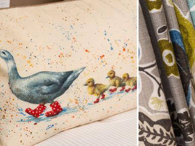 A fabric with a printed design of a goose and three ducklings wearing red polka dot boots next to patterned folded fabrics