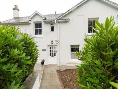 The front entrance of a white house with green bushes on each side and a sign reading Scots Pine in Keswick