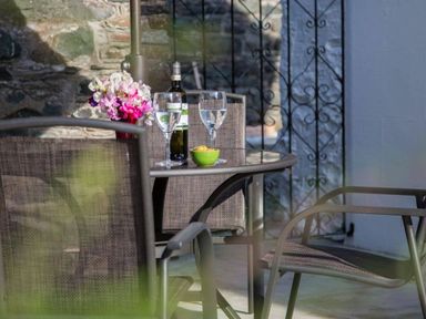 An outdoor patio with a glass table holding a bottle, two wine glasses, a bowl of olives, and a vase of flowers at Scots Pine in Keswick