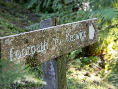 A moss-covered wooden signpost in a forest pointing to a footpath to Keswick