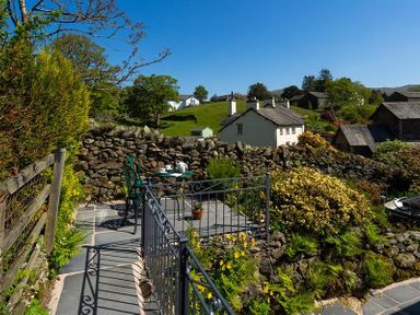 An outdoor seating area with a table and chairs on a stone patio surrounded by stone walls and plants at Corner Cottage in Troutbeck