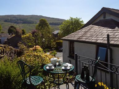 A garden patio with a metal table and chairs set with teacups and binoculars near a house with hills in the background at Corner Cottage in Troutbeck