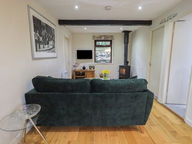 A living room with a green sofa a wood burning stove wooden floor and a TV at Corner Cottage in Troutbeck
