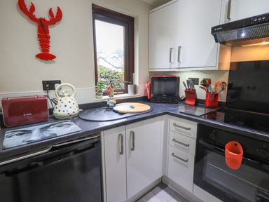 A kitchen with black countertop white cabinets a window a kettle toaster and cooking utensils at Corner Cottage in Troutbeck