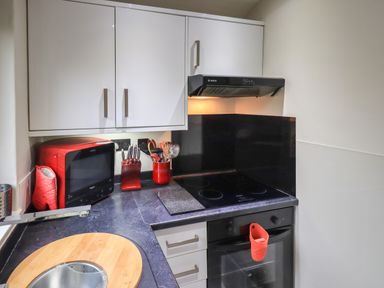A kitchen corner with a black countertop white cabinets a red microwave red utensil holder red knife block and a black stove at Corner Cottage in Troutbeck