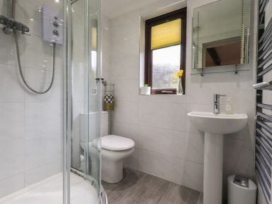 A bathroom with a shower cubicle toilet pedestal sink and a window at Corner Cottage in Troutbeck