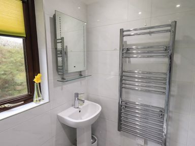 A bathroom sink with a wall mirror a vase with yellow flowers on a window sill and a chrome towel rail at Corner Cottage in Troutbeck