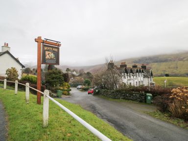 A sign for Mortal Man with buildings and a road in Troutbeck