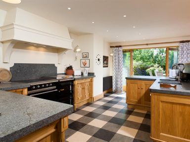 A kitchen with wooden cabinets checkered floor and large glass doors showing a garden at The Old Coach House in Troutbeck