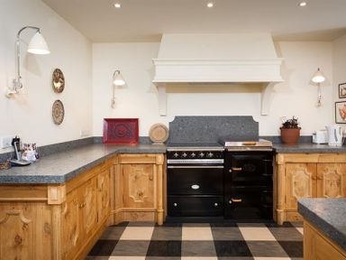 A kitchen with wooden cabinets a black oven checkered floor and countertop appliances at The Old Coach House in Troutbeck