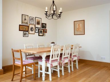 A dining room with a wooden table surrounded by white chairs with cushions and pictures on the wall at The Old Coach House in Troutbeck