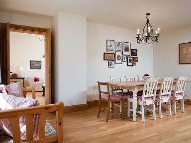 A dining room with a wooden table and chairs with cushions and a chandelier above at The Old Coach House in Troutbeck