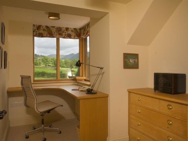 A home office with a wooden desk and chair by a window and a wooden chest of drawers nearby at The Old Coach House in Troutbeck