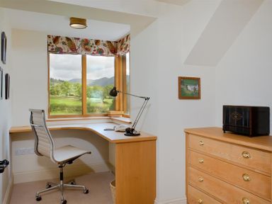 A small office with a corner desk chair and lamp by a window and a chest of drawers with a black box on top at The Old Coach House in Troutbeck
