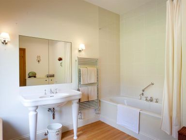 A bathroom with a white sink a bathtub with a shower curtain and towels on a rack at The Old Coach House in Troutbeck