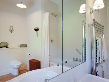 A bathroom with a toilet a bathtub with shower curtain a towel rack with towels and a sink at The Old Coach House in Troutbeck
