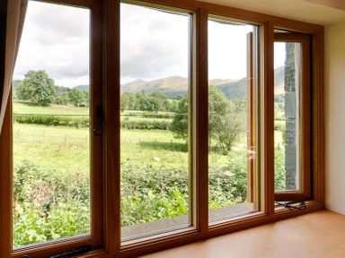 A view through wooden framed windows showing green fields and hills at The Old Coach House in Troutbeck