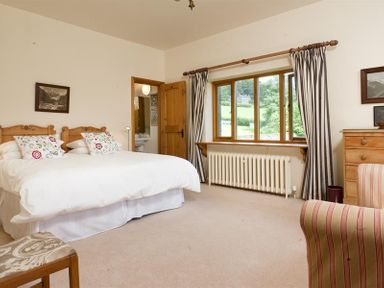 A bedroom with a double bed two pillows a window with striped curtains a wooden dresser and a striped armchair at The Old Coach House in Troutbeck