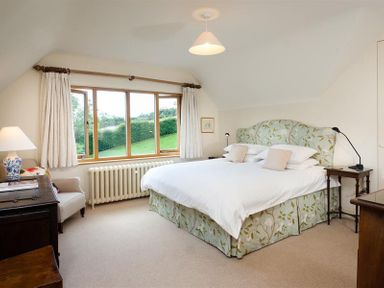 A bedroom with a double bed a side table a lamp a chair and a window overlooking greenery at The Old Coach House in Troutbeck