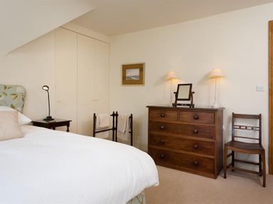 A bedroom with a bed side table and lamp a wooden dresser with two lamps and a mirror a wooden chair and a towel rack at The Old Coach House in Troutbeck