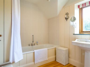 A bathroom with a bathtub a white shower curtain a towel a wicker laundry basket a sink and a window at The Old Coach House in Troutbeck