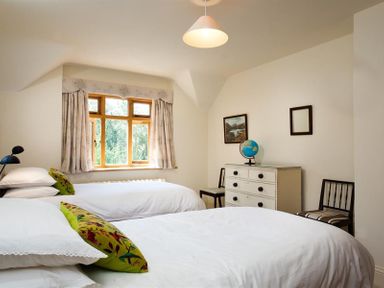 A bedroom with two single beds two chairs a dresser with a globe and framed pictures on the wall at The Old Coach House in Troutbeck