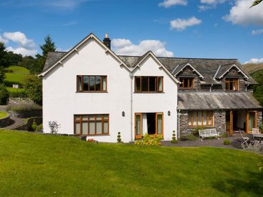 A large two story house with white and stone exterior walls and a green lawn at The Old Coach House in Troutbeck