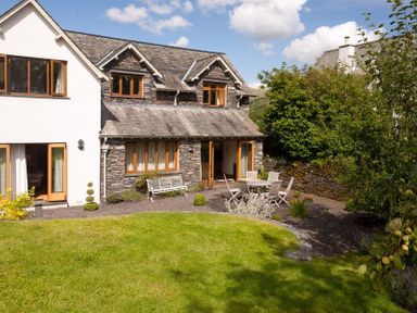 A garden with green lawn outdoor seating and a stone and white house at The Old Coach House in Troutbeck