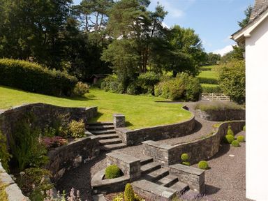 An outdoor garden with stone steps and walls surrounded by grass and trees at The Old Coach House in Troutbeck