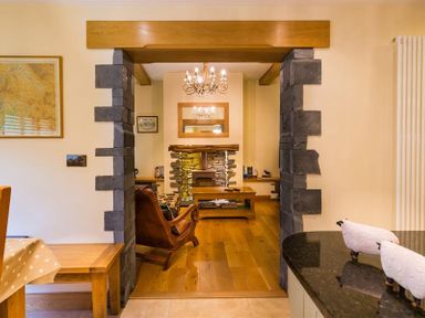 A view from a kitchen with black countertop and sheep figurines to a living room with stone fireplace wooden coffee table and armchair at Oaklea in Ambleside