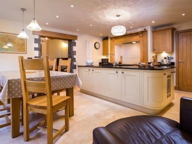 A kitchen with a dining table covered with a polka dot tablecloth and wooden chairs at Oaklea in Ambleside