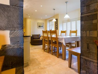 A dining area with a wooden table covered with a polka dot tablecloth and wooden chairs next to windows with shutters at Oaklea Ambleside