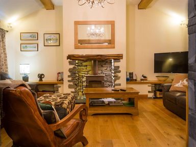 A living room with a stone fireplace wooden coffee table wooden armchair and wall-mounted tv at Oaklea Ambleside