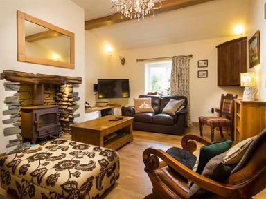 A living room with a wood burning stove a patterned ottoman and a leather sofa at Oaklea in Ambleside
