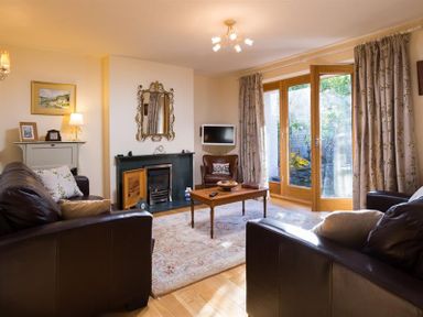A living room with brown leather sofas a wooden coffee table a fireplace a mirror and glass doors at Oaklea in Ambleside