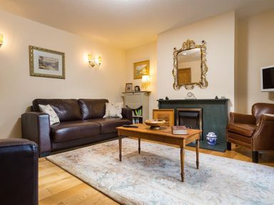 A living room with a brown leather sofa a wooden coffee table an armchair and a fireplace at Oaklea in Ambleside