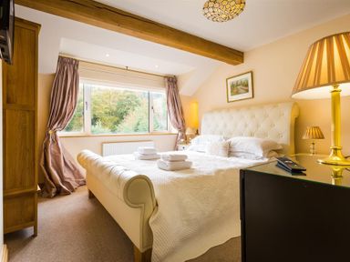 A bedroom with a large upholstered bed towels on the bed wooden furniture and a window with curtains at Oaklea in Ambleside