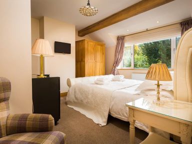A bedroom with a bed folded towels wooden wardrobe armchair and lamps at Oaklea Ambleside