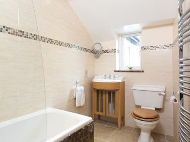 A bathroom with a bathtub a wooden vanity sink a toilet a towel rack and a window at Oaklea in Ambleside