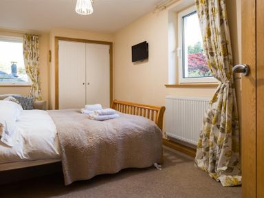 A bedroom with a bed towels on the bed wall-mounted television and floral curtains at Oaklea in Ambleside