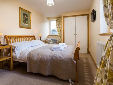 A bedroom with a wooden bed and bedside tables a chair curtains and a wall-mounted television at Oaklea in Ambleside
