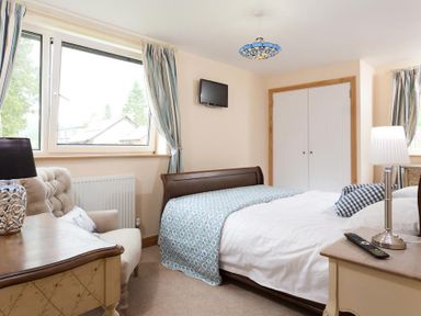 A bedroom with a bed a chair a desk a wall mounted tv and a closet at Oaklea in Ambleside